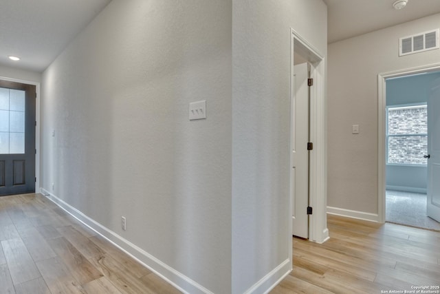 corridor with light wood-style flooring, visible vents, and baseboards