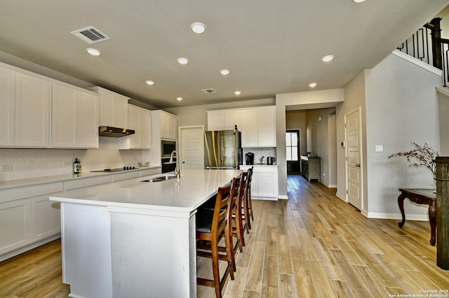 kitchen featuring light countertops, visible vents, freestanding refrigerator, white cabinets, and a sink