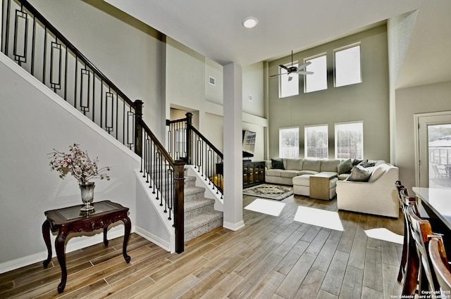 living room featuring a ceiling fan, visible vents, stairway, and light wood finished floors