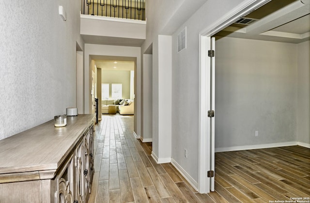 hallway with wood finish floors, visible vents, and baseboards