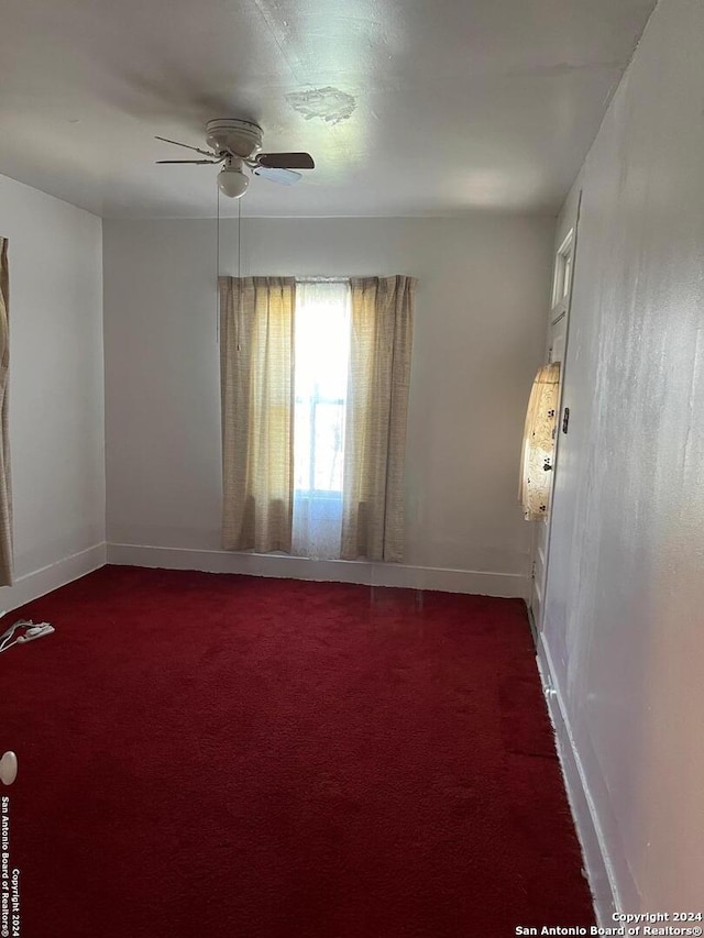 spare room featuring baseboards, dark carpet, and a ceiling fan