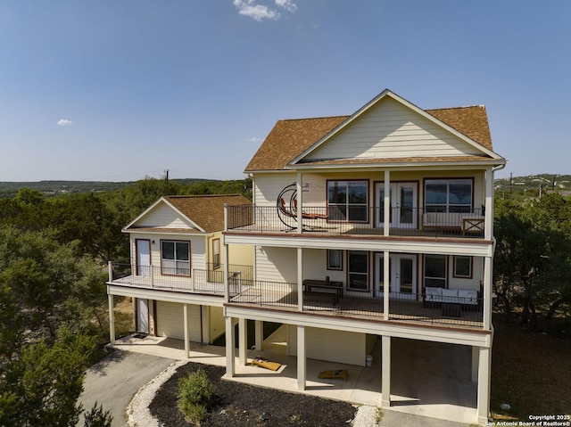 rear view of property with a patio, a balcony, a garage, driveway, and roof with shingles