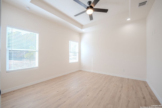 spare room with ceiling fan, light wood-style flooring, visible vents, baseboards, and a raised ceiling