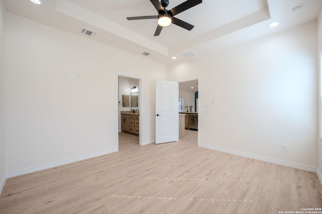 unfurnished bedroom with light wood-style flooring, a raised ceiling, visible vents, and baseboards