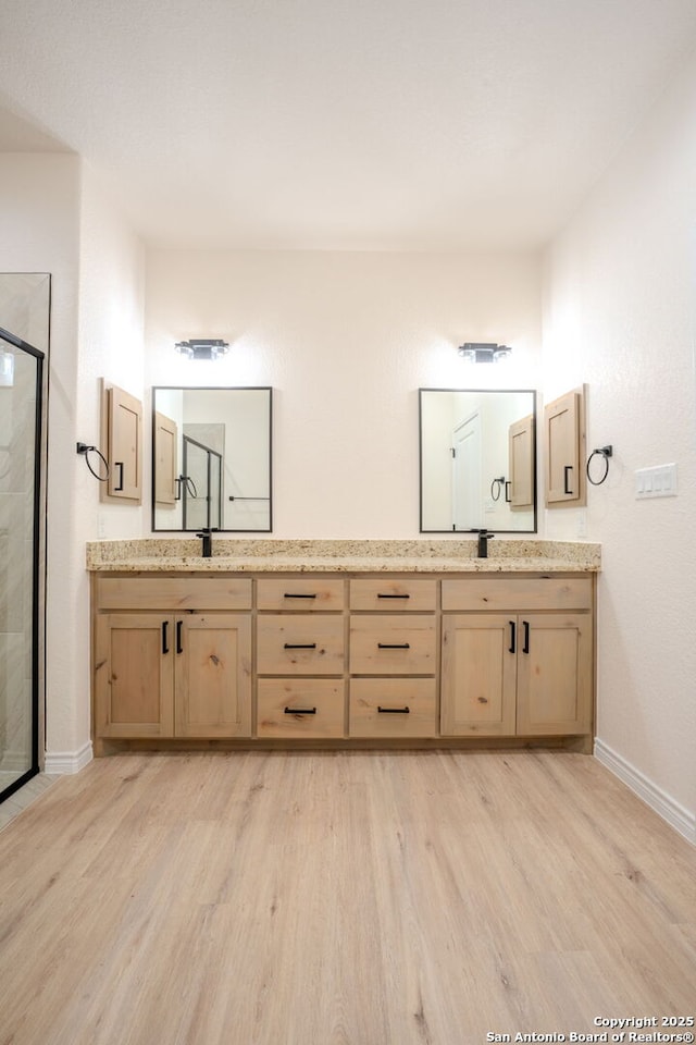 full bath featuring double vanity, a shower stall, baseboards, and wood finished floors