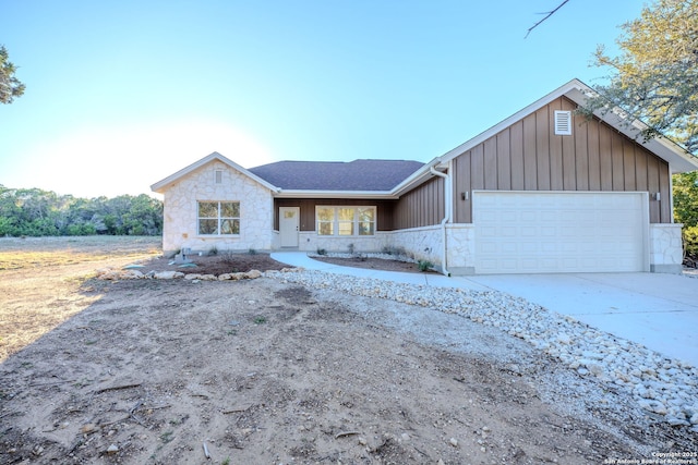 view of front of house with a shingled roof, concrete driveway, stone siding, an attached garage, and board and batten siding