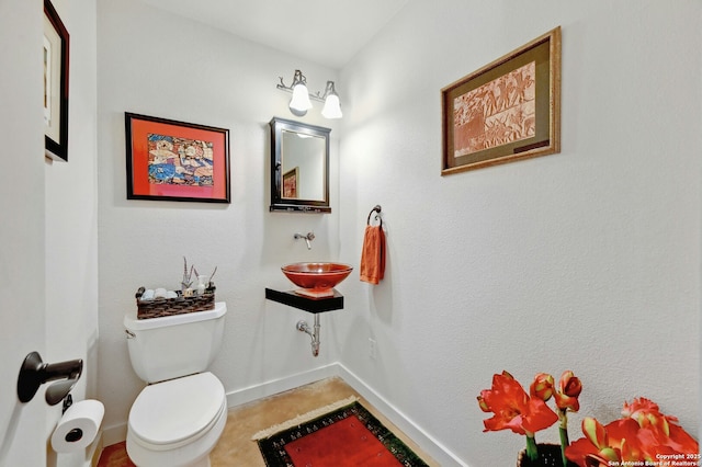 half bath featuring baseboards and toilet