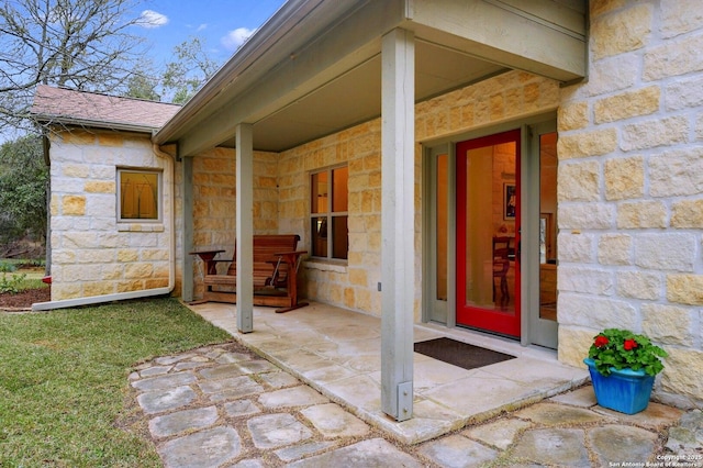 doorway to property with a porch, stone siding, and roof with shingles