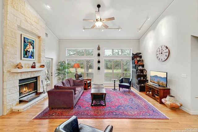 living room with a stone fireplace, track lighting, wood finished floors, high vaulted ceiling, and baseboards