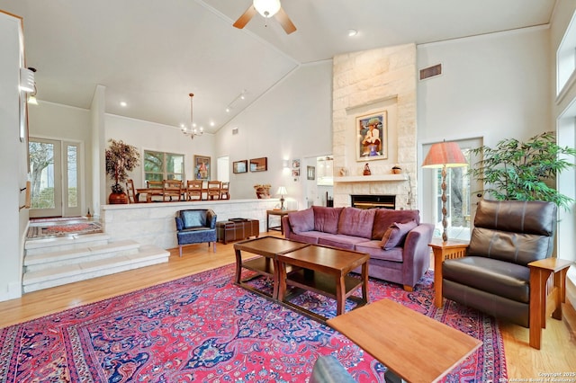 living area with high vaulted ceiling, a stone fireplace, ceiling fan with notable chandelier, visible vents, and light wood-type flooring