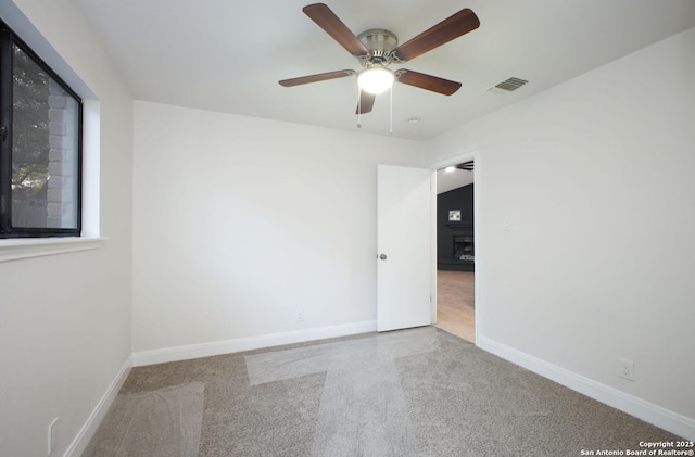 unfurnished room featuring a ceiling fan, a fireplace, visible vents, and baseboards