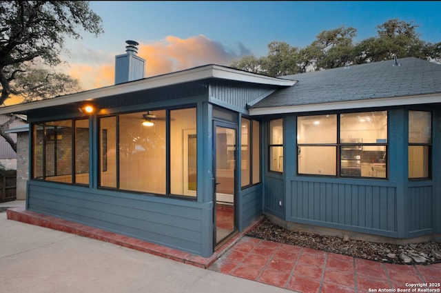 exterior space with a sunroom, a shingled roof, a chimney, and a patio