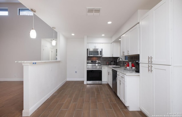 kitchen featuring pendant lighting, stainless steel appliances, light countertops, white cabinetry, and a sink