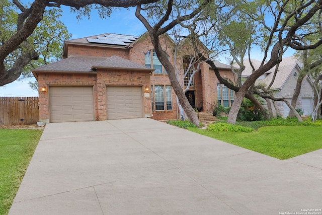 traditional-style home with a garage, brick siding, fence, driveway, and roof mounted solar panels