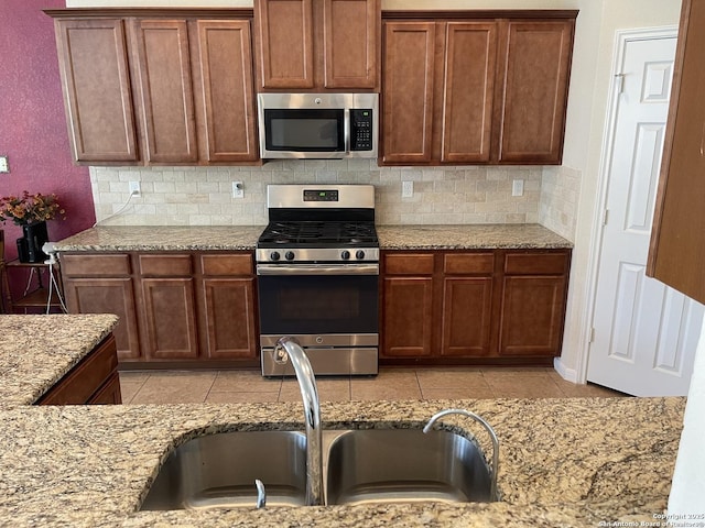 kitchen featuring light stone counters, light tile patterned floors, decorative backsplash, appliances with stainless steel finishes, and a sink