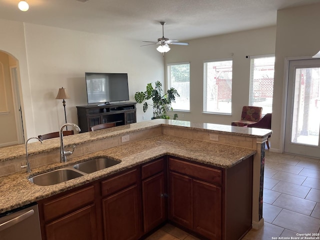 kitchen featuring light tile patterned floors, arched walkways, open floor plan, stainless steel dishwasher, and a sink