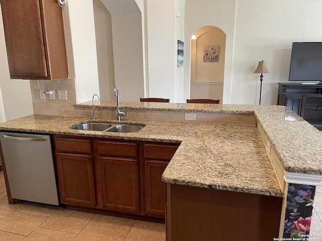 kitchen featuring a sink, light stone countertops, arched walkways, and stainless steel dishwasher