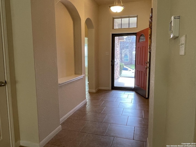 foyer entrance featuring arched walkways, baseboards, and tile patterned floors