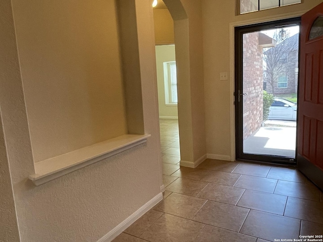 foyer featuring arched walkways, plenty of natural light, light tile patterned flooring, and baseboards