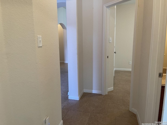 hallway with dark tile patterned floors, arched walkways, and baseboards