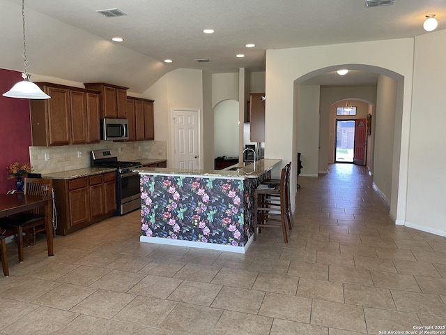 kitchen with arched walkways, decorative light fixtures, stainless steel appliances, visible vents, and a peninsula