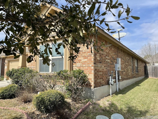 view of side of home with a yard, brick siding, fence, and an attached garage