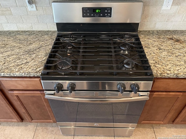 room details featuring stone counters, tasteful backsplash, brown cabinets, and gas range