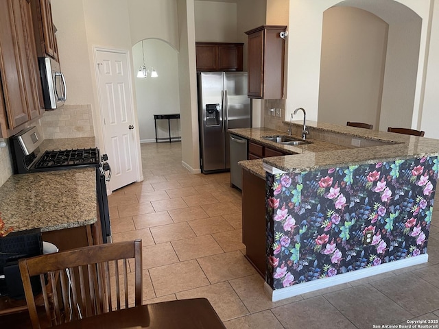 kitchen with arched walkways, light stone counters, stainless steel appliances, a peninsula, and a sink