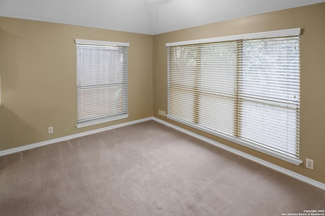 carpeted spare room featuring lofted ceiling, baseboards, and a healthy amount of sunlight