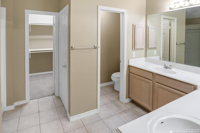 bathroom with a walk in closet, toilet, vanity, baseboards, and tile patterned floors