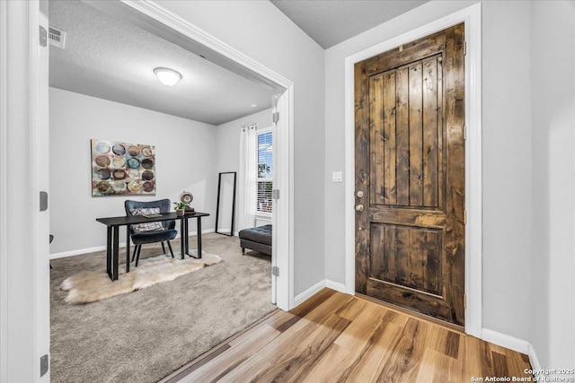 carpeted foyer with a textured ceiling, wood finished floors, visible vents, and baseboards