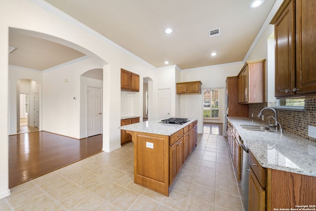 kitchen featuring a kitchen island, visible vents, a sink, light stone countertops, and brown cabinetry