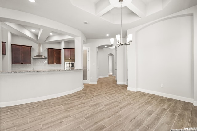 unfurnished living room with baseboards, arched walkways, an inviting chandelier, light wood-style floors, and recessed lighting