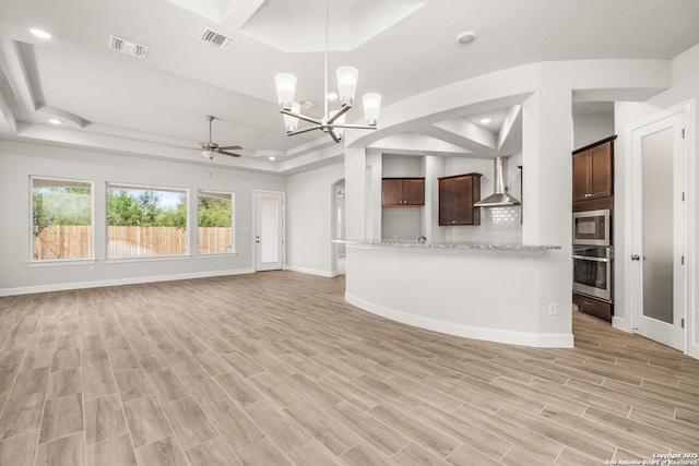 kitchen with light stone counters, a tray ceiling, appliances with stainless steel finishes, open floor plan, and wall chimney range hood