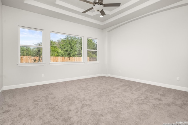 carpeted empty room featuring ceiling fan, a tray ceiling, and baseboards