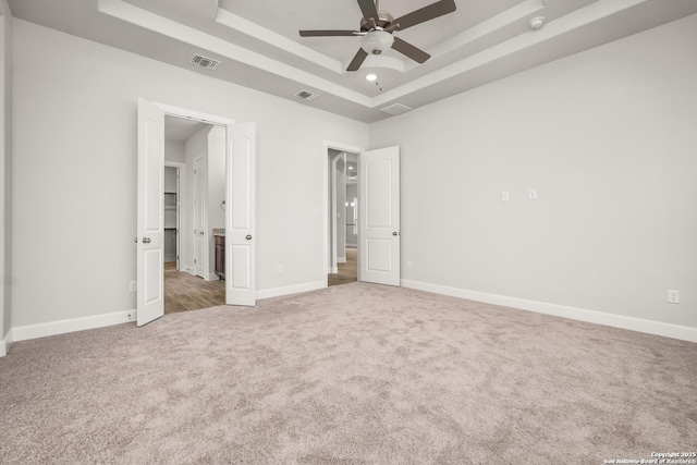 unfurnished bedroom with a tray ceiling, carpet flooring, visible vents, and baseboards