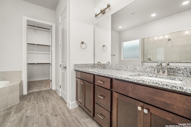 bathroom featuring double vanity, tiled bath, a sink, and tiled shower