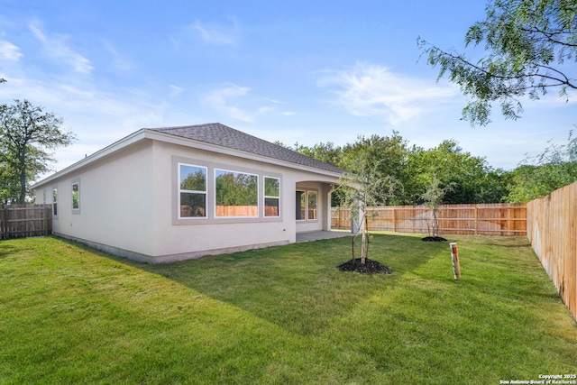 rear view of house featuring a fenced backyard, a shingled roof, a lawn, and stucco siding