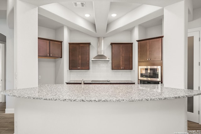 kitchen with wall chimney range hood, stainless steel microwave, visible vents, and light stone countertops