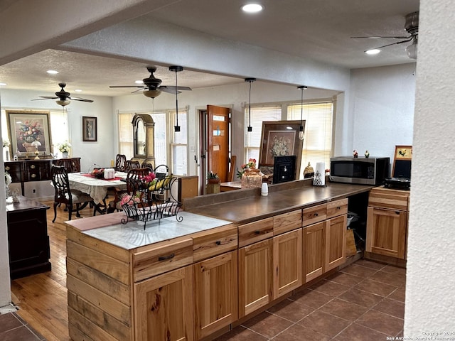 kitchen featuring a ceiling fan, stainless steel microwave, brown cabinets, decorative light fixtures, and a textured ceiling