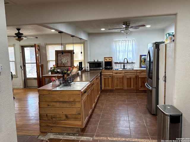 kitchen with dark countertops, appliances with stainless steel finishes, a peninsula, hanging light fixtures, and a sink