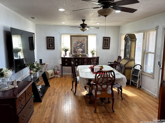 dining space with light wood-type flooring, baseboards, visible vents, and a textured ceiling