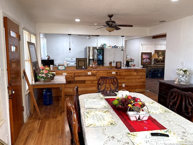 dining space with a textured ceiling, visible vents, wood finished floors, and a ceiling fan