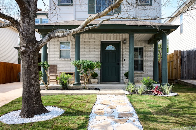 doorway to property with a porch, brick siding, fence, and a lawn