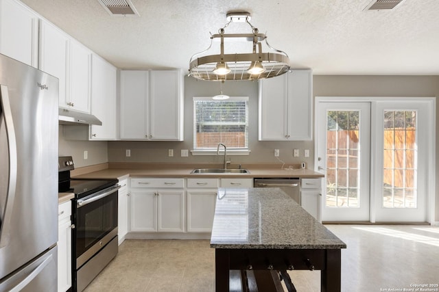 kitchen featuring white cabinets, stainless steel appliances, under cabinet range hood, pendant lighting, and a sink