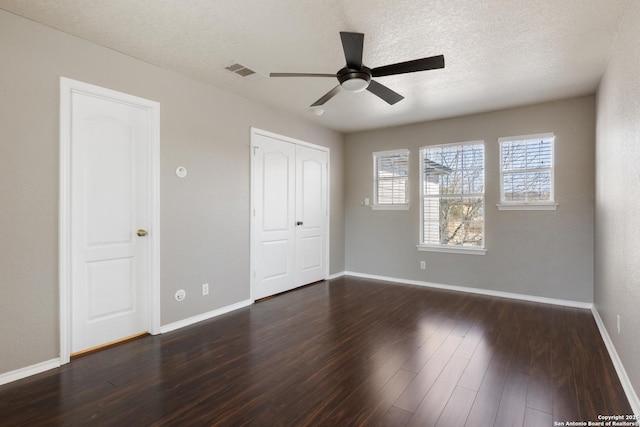 unfurnished bedroom with visible vents, dark wood finished floors, a textured ceiling, and baseboards