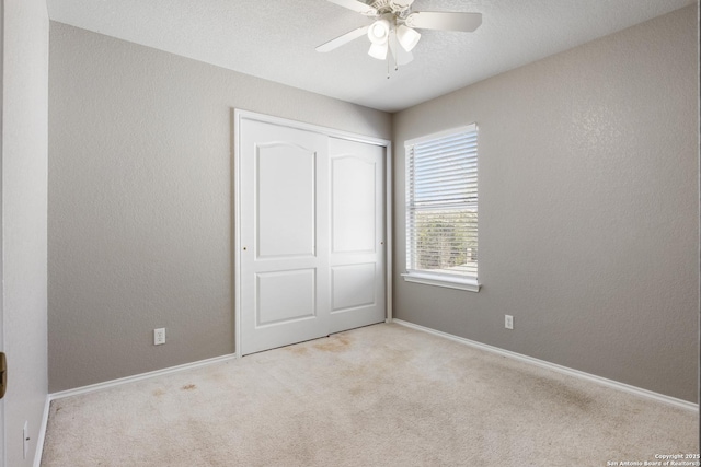 unfurnished bedroom with light carpet, a textured wall, a closet, and baseboards