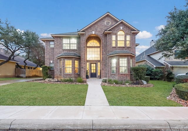 traditional-style house featuring brick siding, a front lawn, and fence