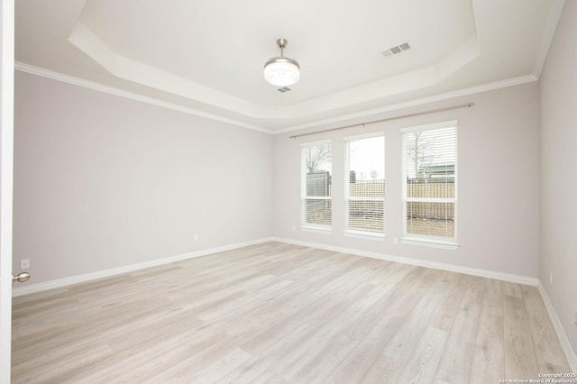 spare room with light wood-type flooring, a raised ceiling, visible vents, and baseboards