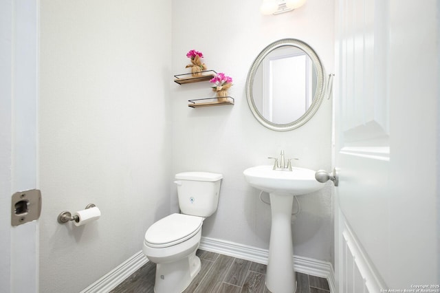 half bathroom with wood finish floors, toilet, and baseboards